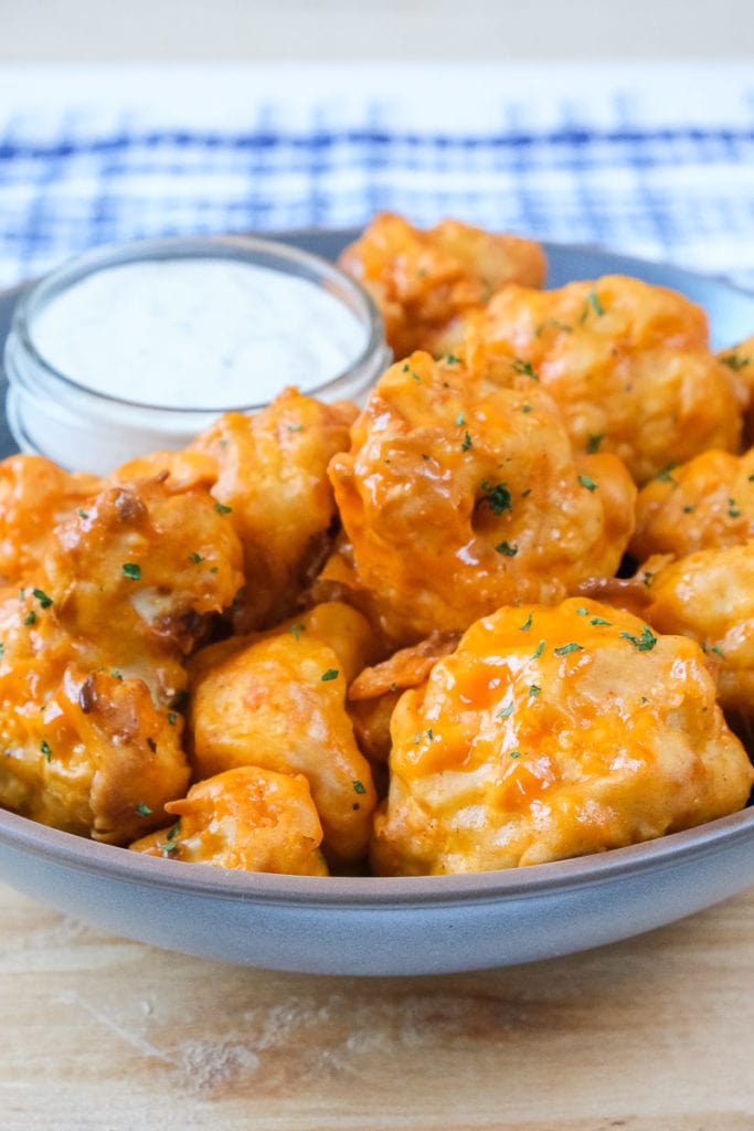 orange cauliflower wings covered in sauce in bowl with dipping sauce beside