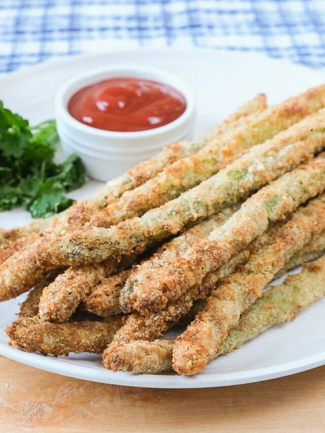 breaded asparagus fries on white plate with ketchup behind