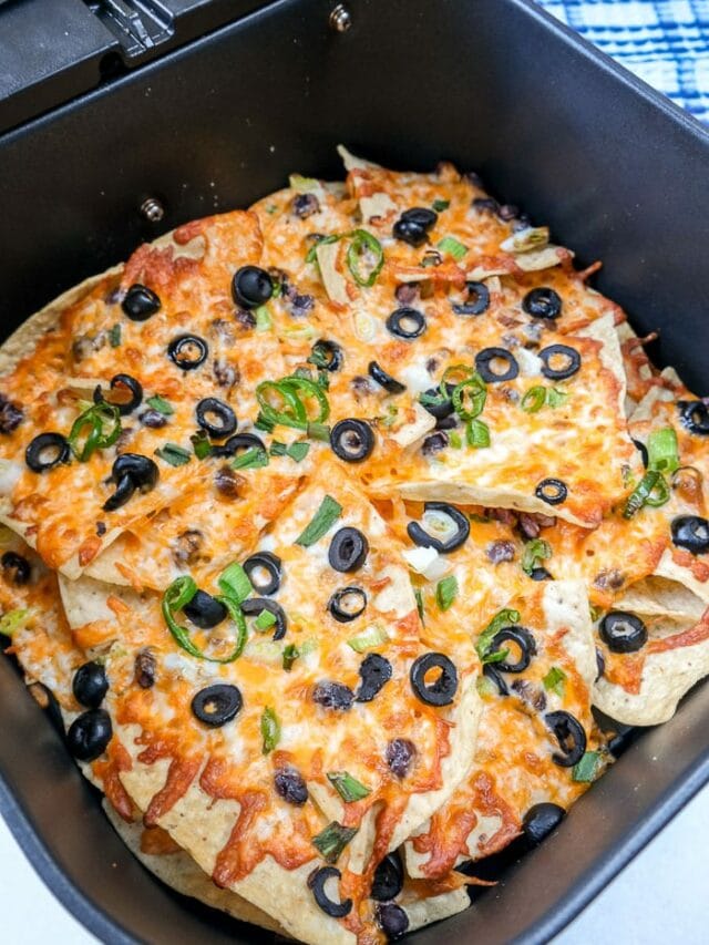 melted cheesy nachos in black air fryer tray on counter top.