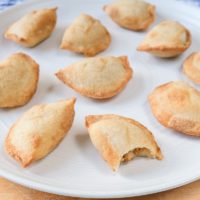 mini empanadas with bite out on white plate on wooden board