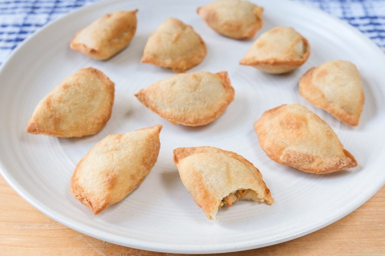 mini empanadas with bite out on white plate on wooden board