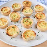 mini quiche with parsley on white plate on wooden board