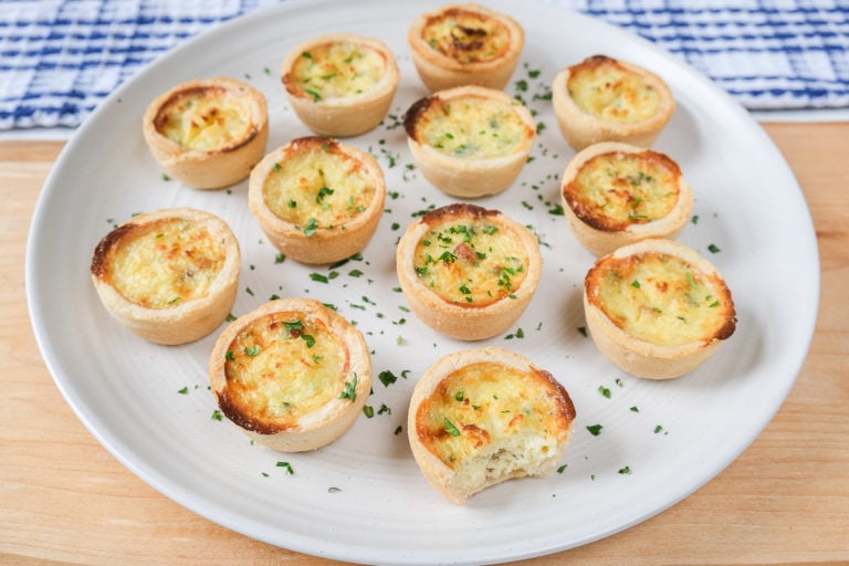 mini quiche with parsley on white plate on wooden board