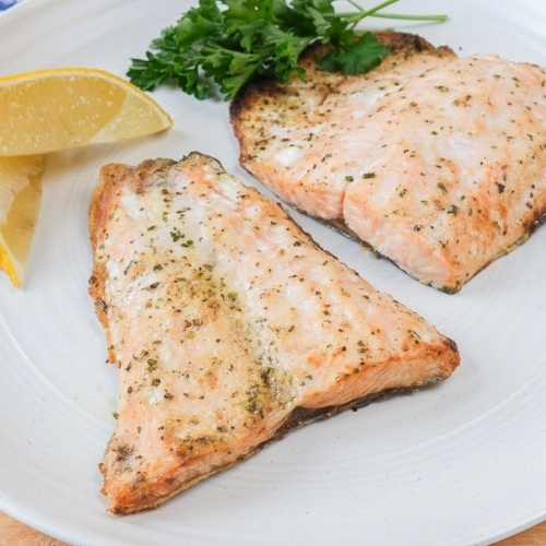 cooked salmon fillets on white plate with lemons beside