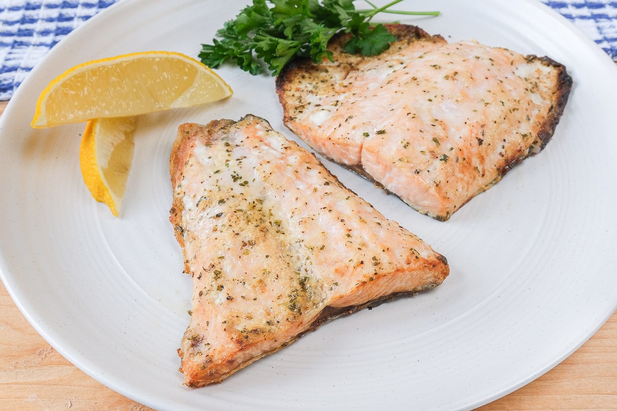 cooked salmon fillets on white plate with lemons beside