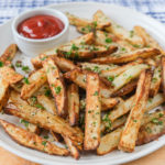 parmesan fries with ketchup for dipping on white platter on wooden board
