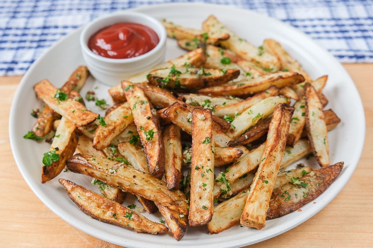 parmesan fries with ketchup for dipping on white platter on wooden board