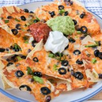 large plate of nachos with sour cream salsa and guacamole on top