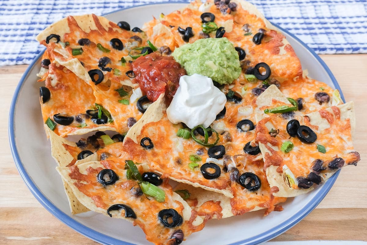 large plate of nachos with sour cream salsa and guacamole on top