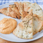 pita chips on plate with orange hummus beside