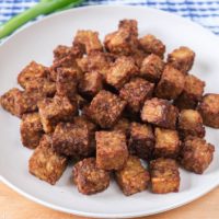 white plate of tempeh cubes on wooden board