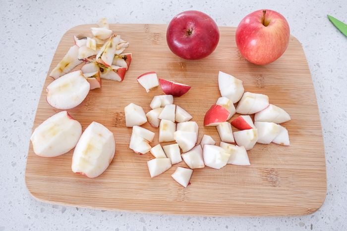 red apples cut into pieces on wooden cutting board on white counter