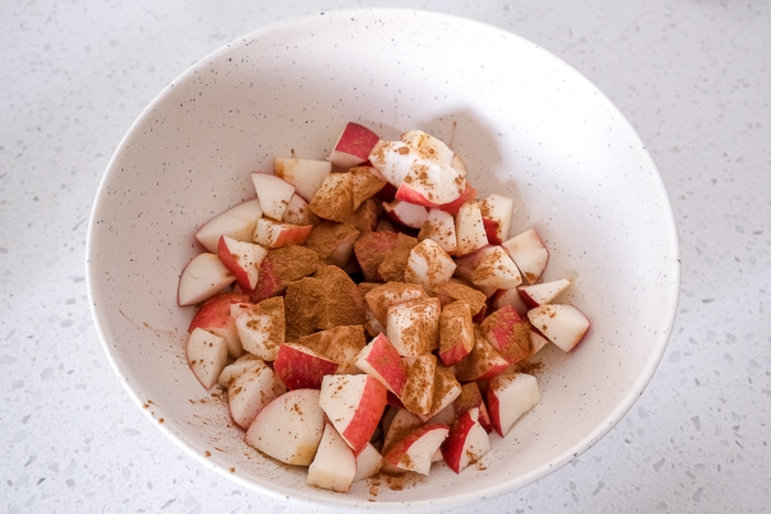 apple pieces covered in cinnamon in white mixing bowl on white counter top