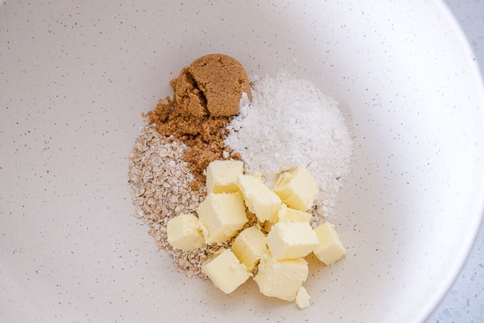 pieces of butter in white bowl with sugar and oats on white counter