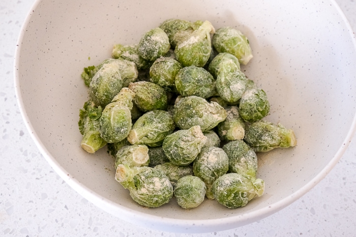 frozen brussels sprouts in white mixing bowl with oil and spices