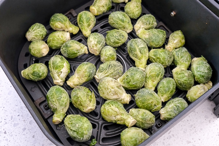 frozen brussels sprouts in black air fryer tray on white counter top