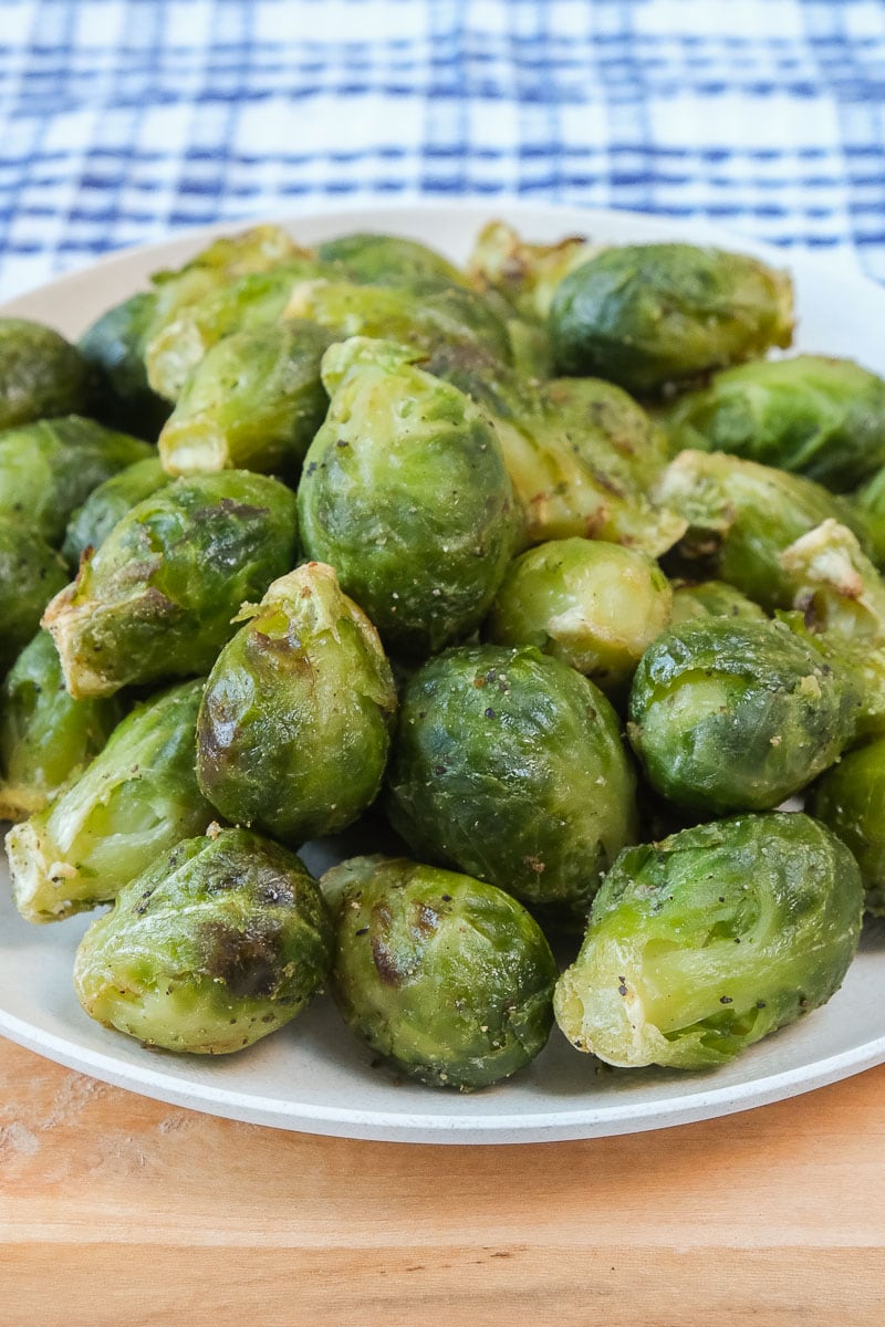 green brussels sprouts on white plate sitting on wooden board