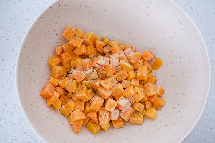 frozen butternut squash pieces with spices in white mixing bowl on counter