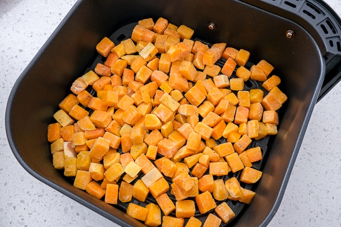 butternut squash pieces in black air fryer tray on white counter