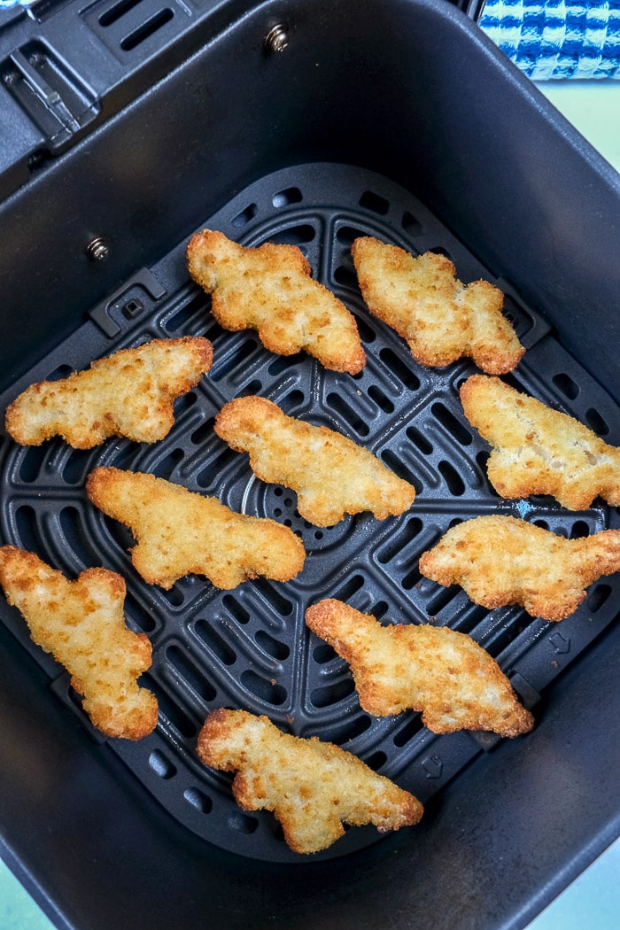 cooked dino nuggets in black air fryer tray on counter top