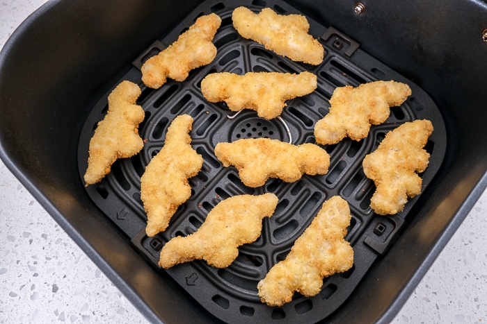 frozen dino nuggets in black air fryer tray on white counter