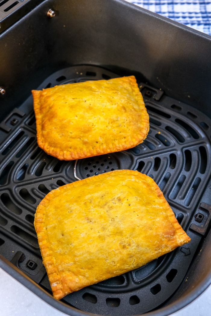 two yellow cooked beef patties in black air fryer tray on counter top