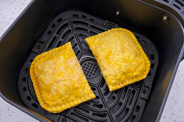 two jamaican beef patties in black air fryer tray on white counter