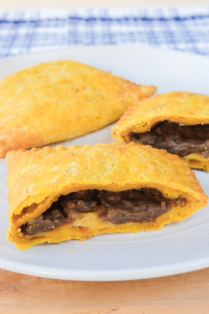 jamaican beef patty cut in half on white plate on wooden board