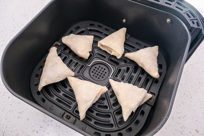 frozen samosas in black air fryer tray on white counter