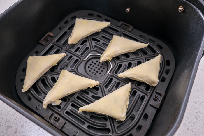 frozen uncooked spanakopita in black air fryer tray on white counter