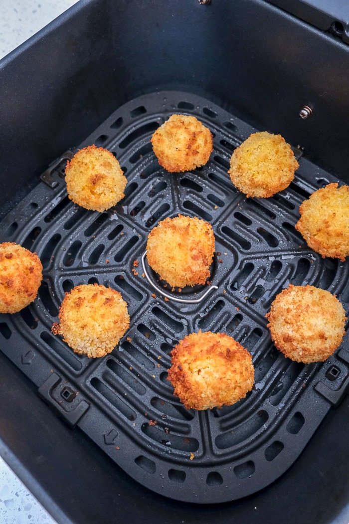 cooked mac and cheese balls in black air fryer tray on counter