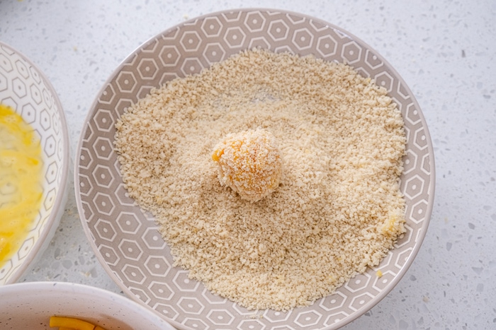 mac and cheese ball in bowl of breadcrumbs on white countertop