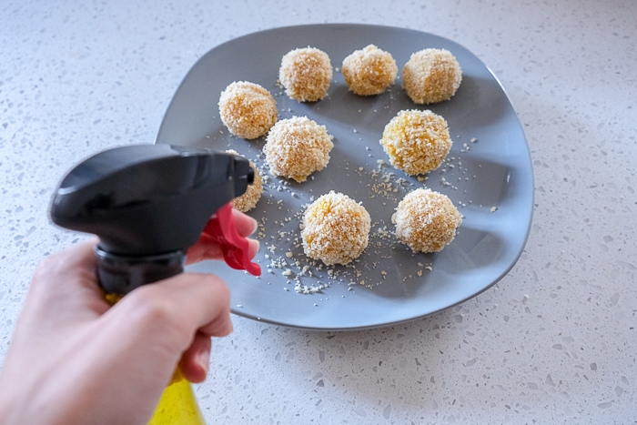 mac and cheese balls on grey plate with oil spray bottle in front