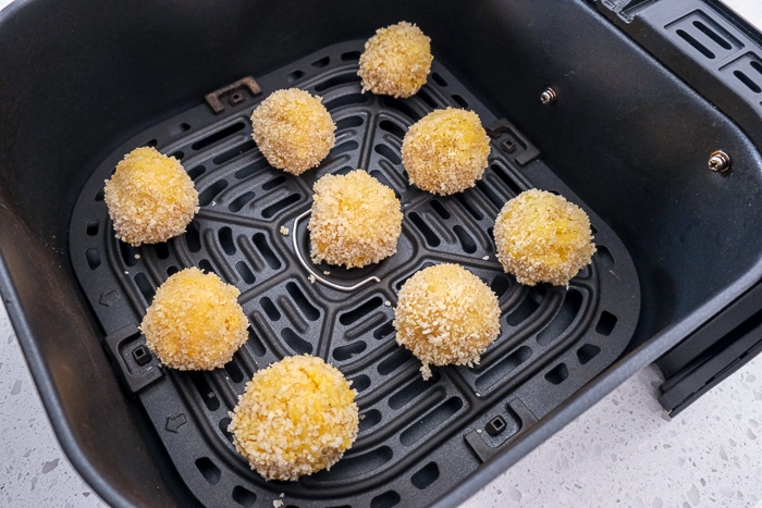 uncooked mac and cheese balls in black air fryer tray on counter