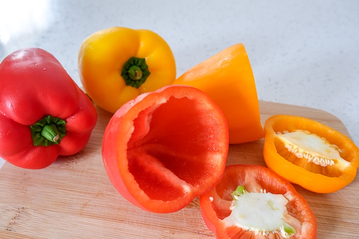 colorful bell peppers with tops cut off on wooden cutting board