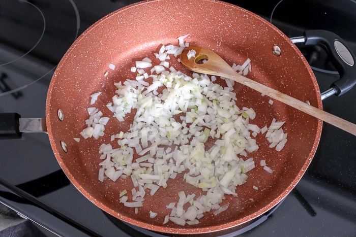 diced onions in large pan on stove top with wooden spoon stirring