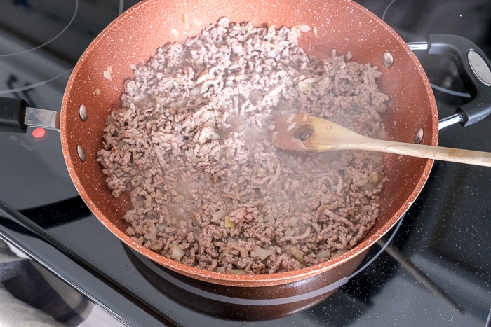 minced beef in red pan on stove top stirred with wooden spoon