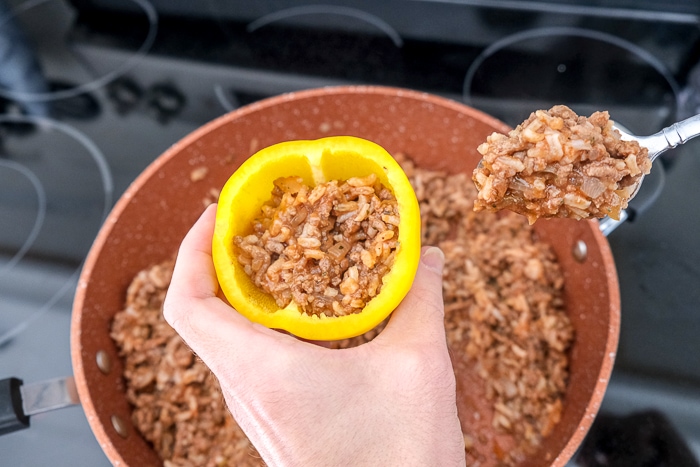 hand holding yellow bell pepper stuffing it with meat and rice blend