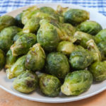 small white plate of green brussels sprouts on wooden board with blue cloth behind