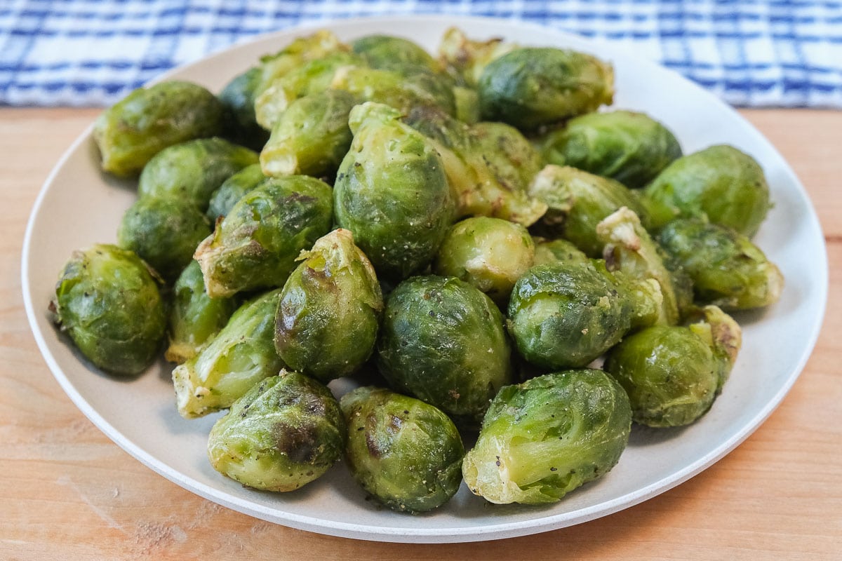 small white plate of green brussels sprouts on wooden board with blue cloth behind