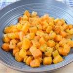 orange cubes of butternut squash in blue bowl on wooden board