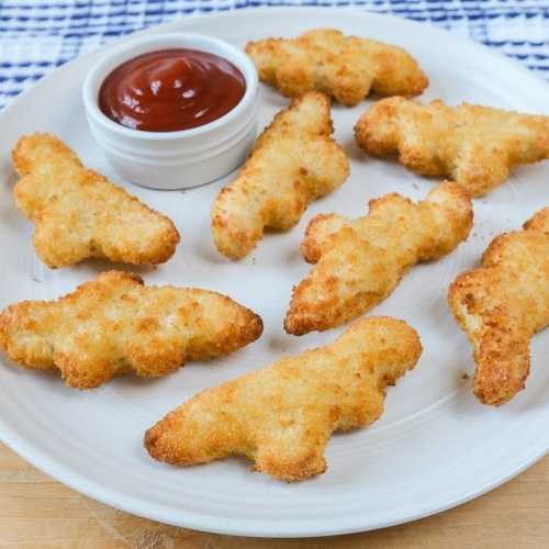 dinosaur shaped nuggets on white plate with ketchup beside