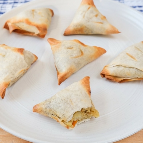 cooked samosas on white plate on wooden board