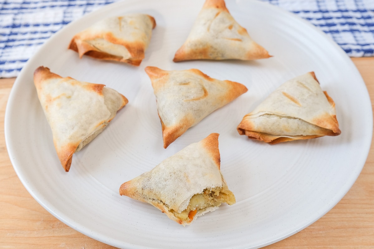 cooked samosas on white plate on wooden board