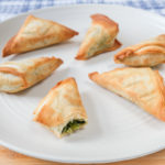 crispy spanakopita on white plate on wooden board