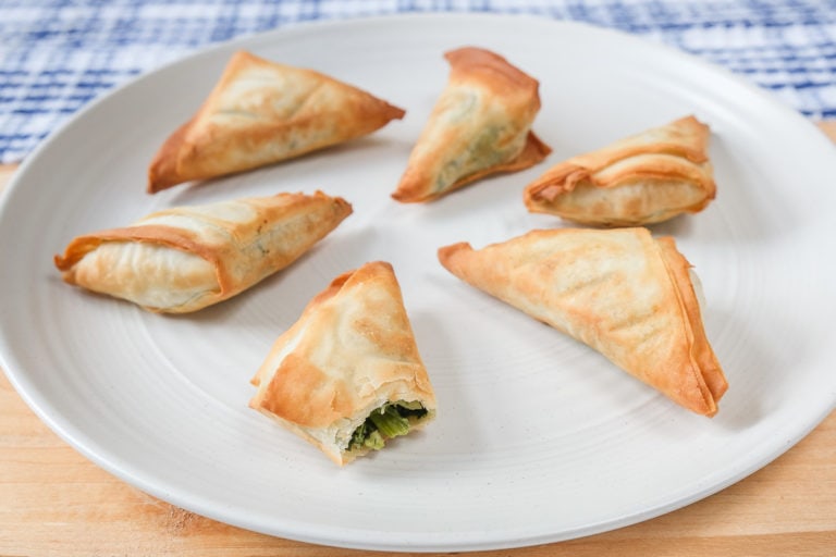 crispy spanakopita on white plate on wooden board