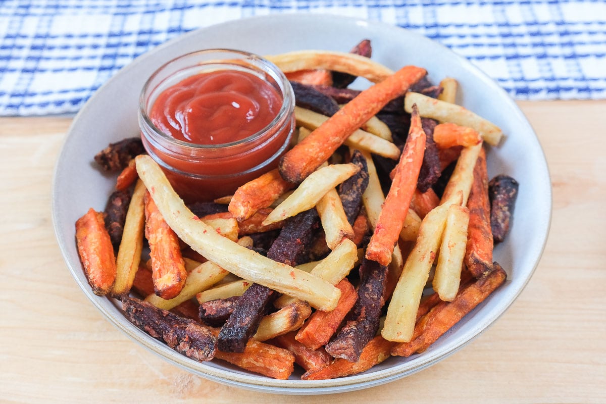 colorful veggie fries in bowl with ketchup on wooden board