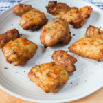 cooked chicken thighs on white plate on wooden board