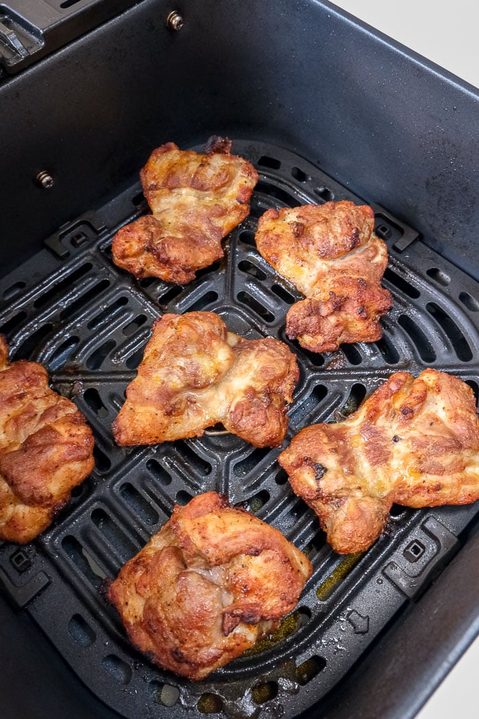 cooked chicken thighs in black air fryer tray on counter top