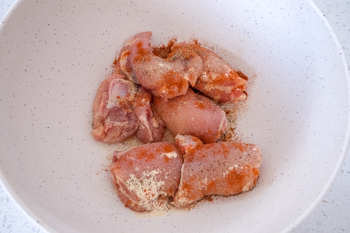 uncooked chicken thighs with spices on top in white bowl